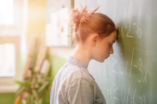 teen with anxiety with head on blackboard and eyes shut