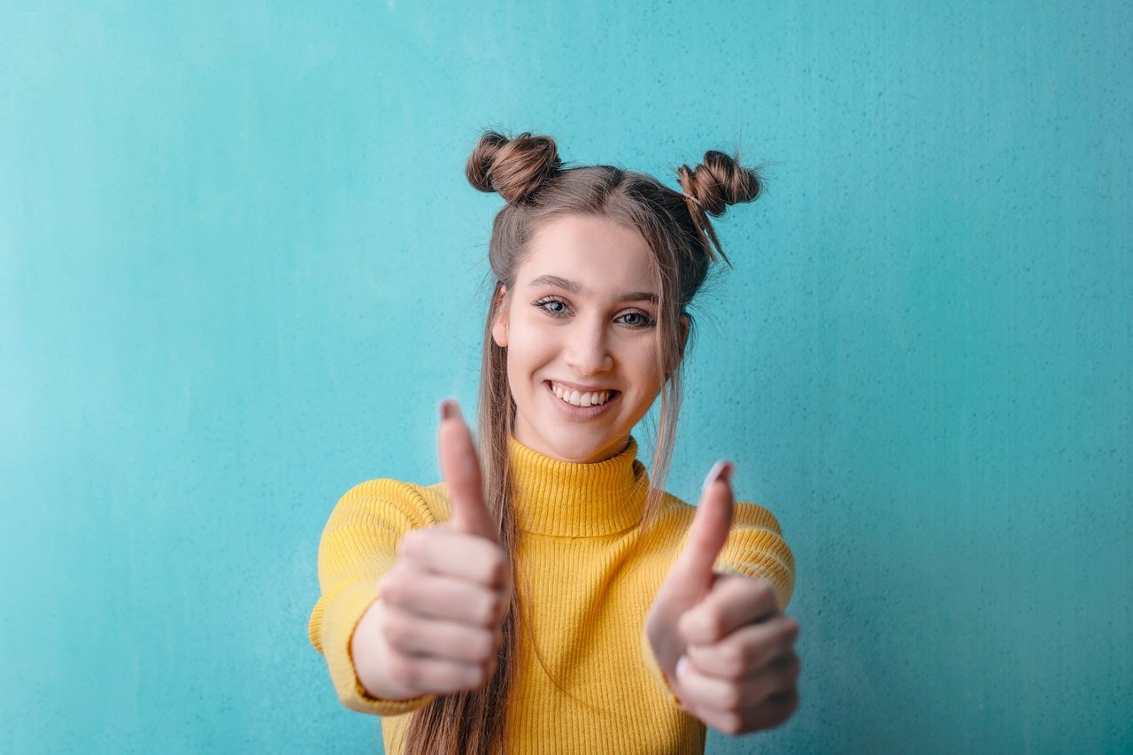 woman in front of blue wall with two thumbs up smiling