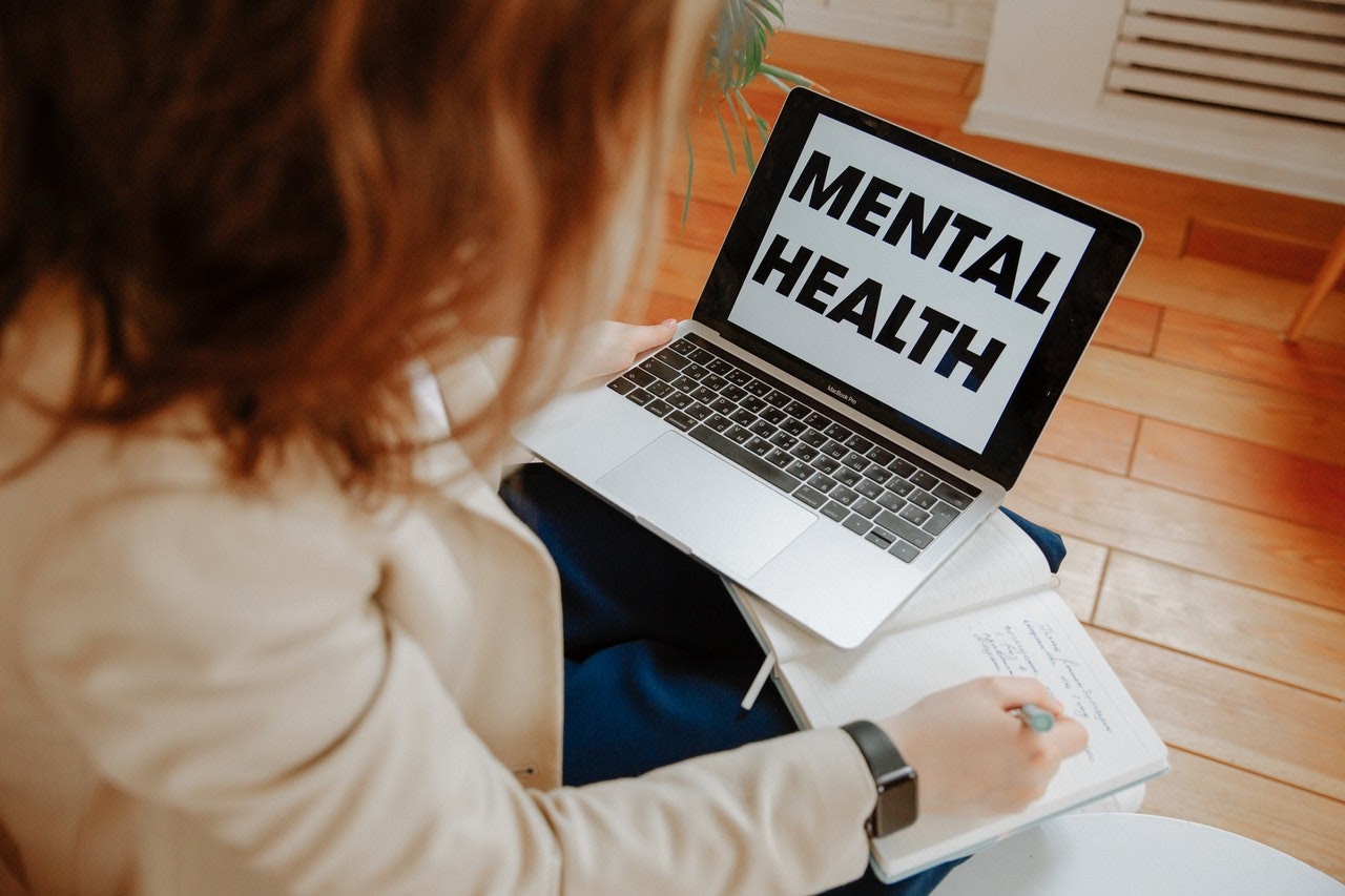 woman taking notes off a laptop with mental health on screen