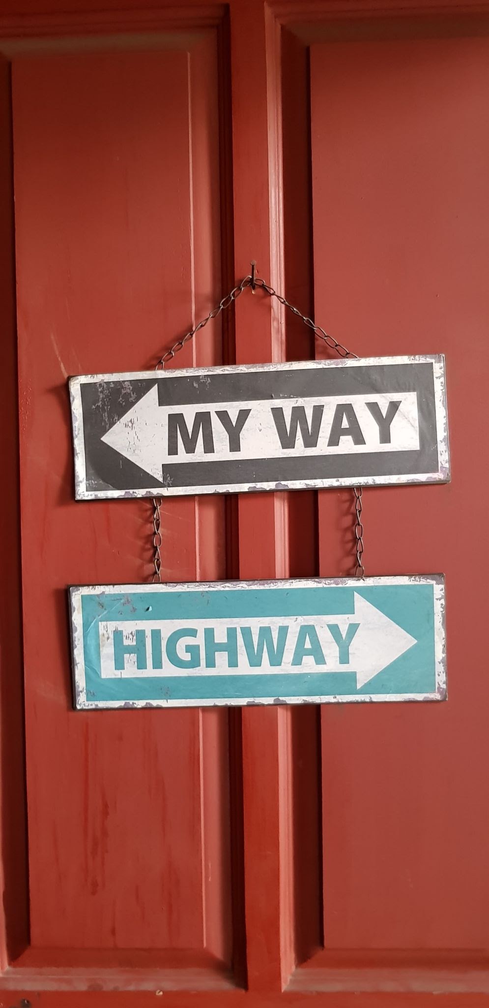 "My way" left facing arrow sign over a "highway" right facing arrow sign in front of a red door.