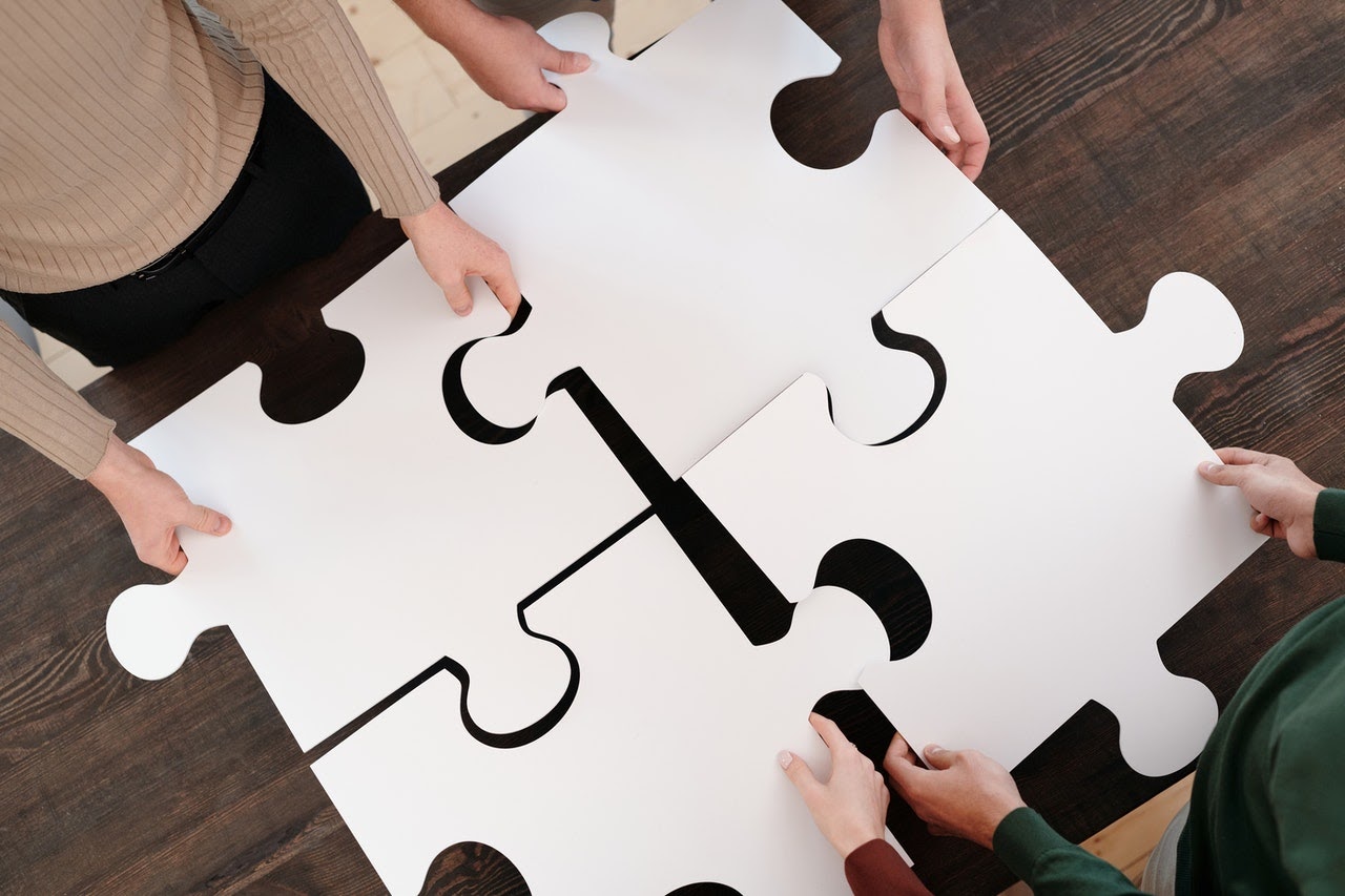 4 people holding puzzle pieces which fit together. 