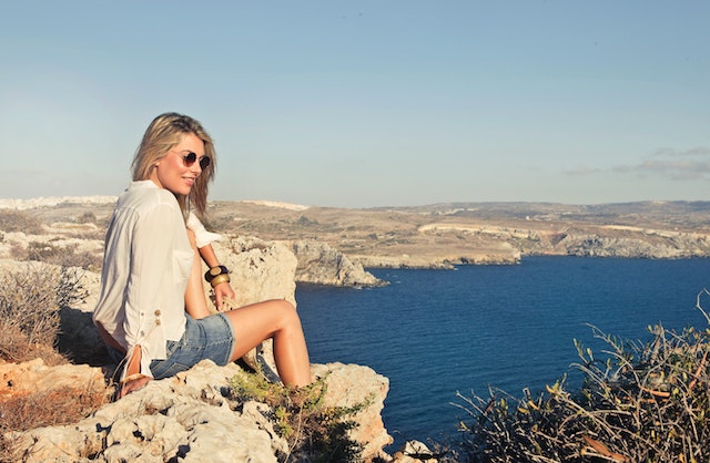 smiling woman sitting on top of a rock overlooking water