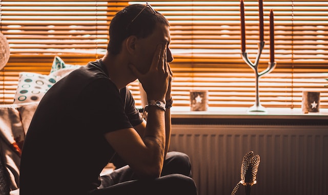 photo of a silhouette of a man sitting on couch holding head in hands who looks stressed