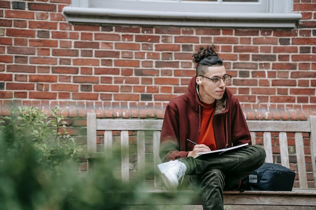 photo of a young adult male sitting on a bench writing in a notepad